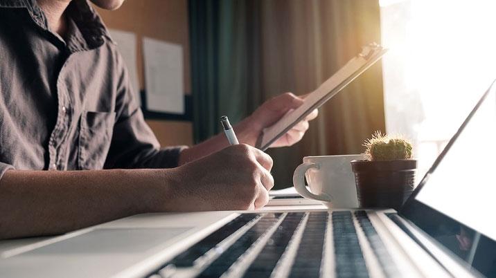 Someone writing notes while sitting at a laptop