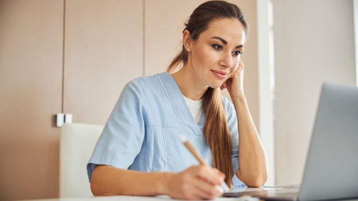 Person in scrubs in front of laptop taking notes