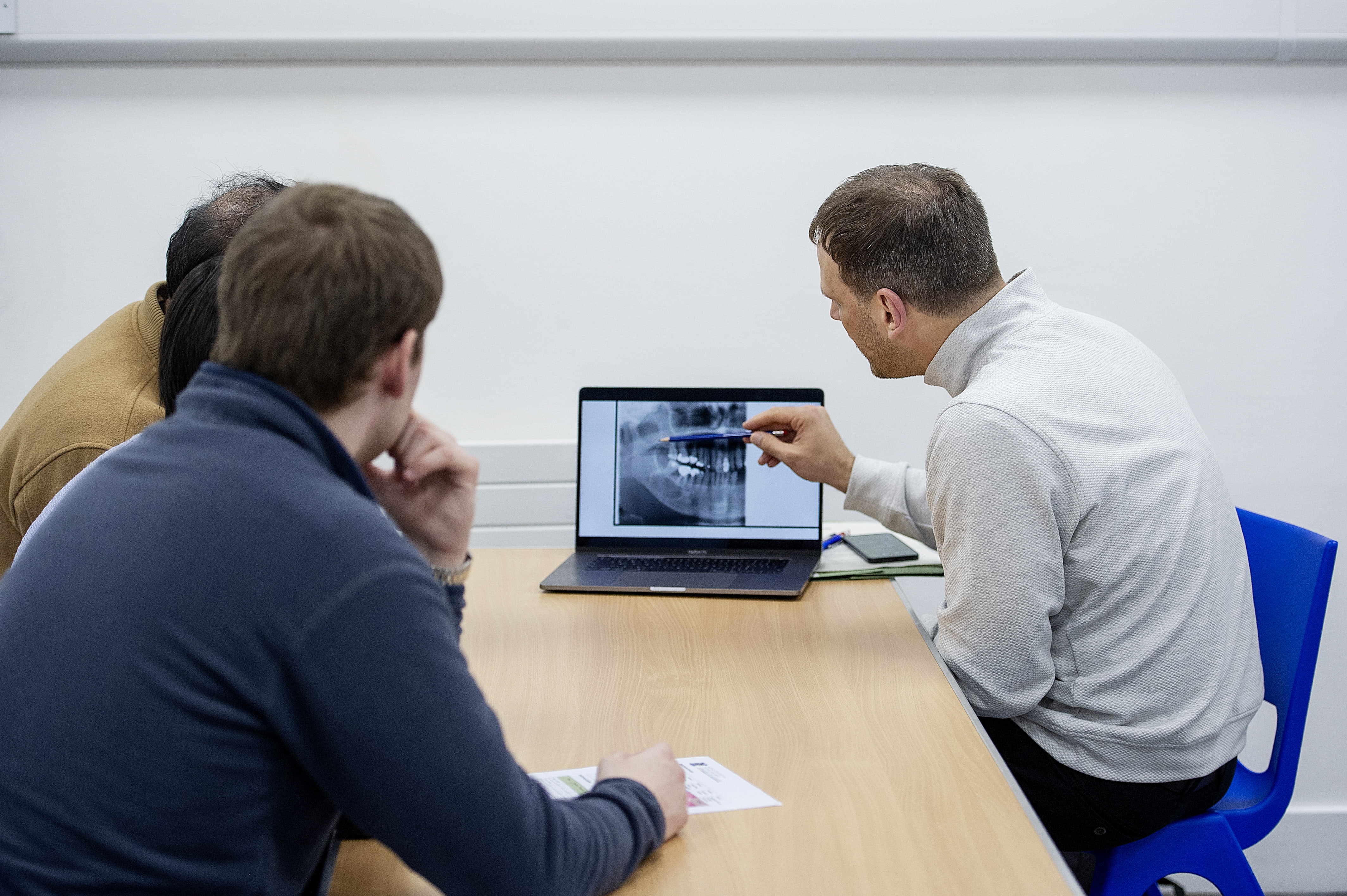 three people looking at a laptop with one describing a dental x-ray to the other two 