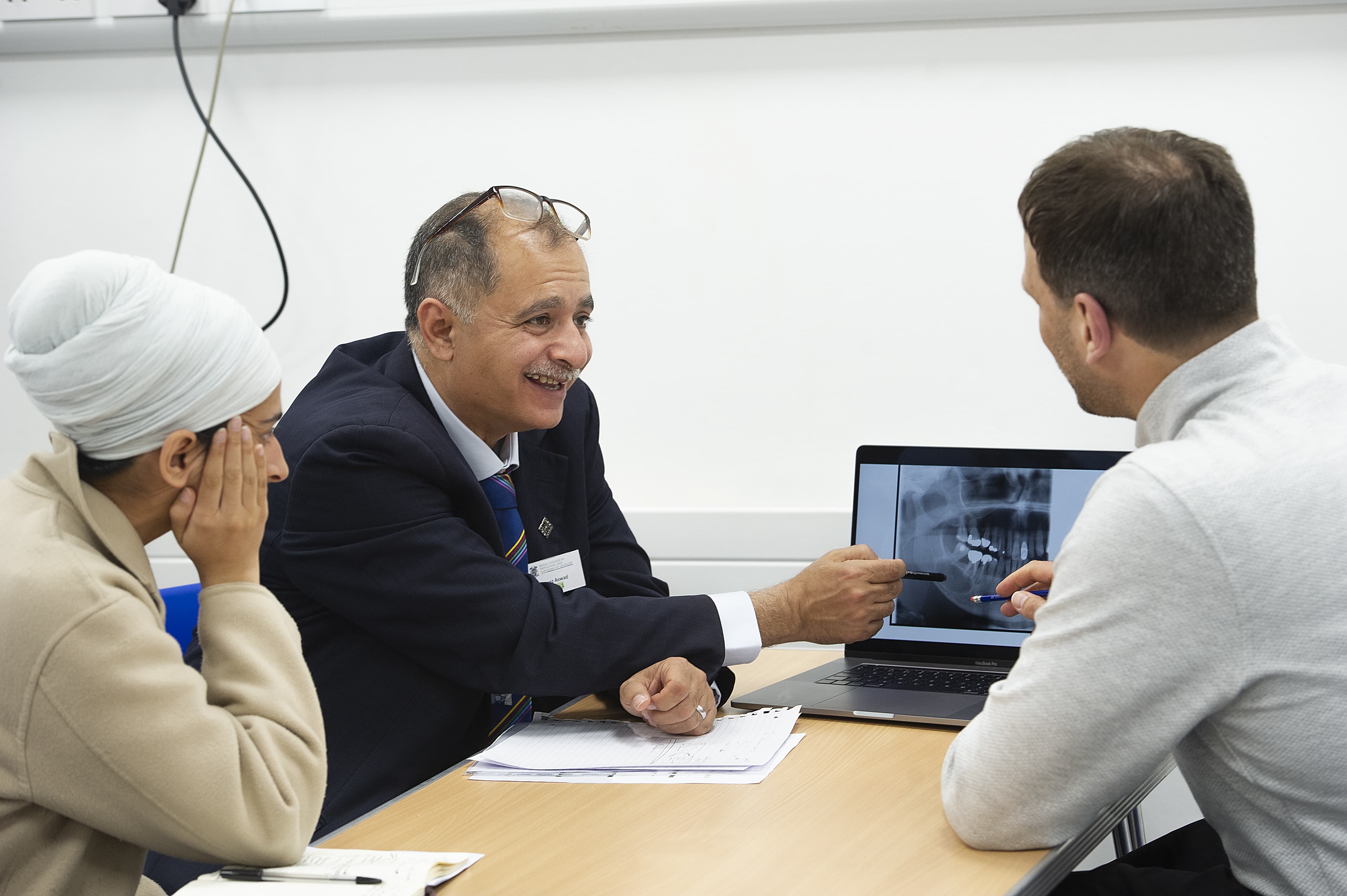 three people looking at and engaging with a laptop that has a dental x-ray