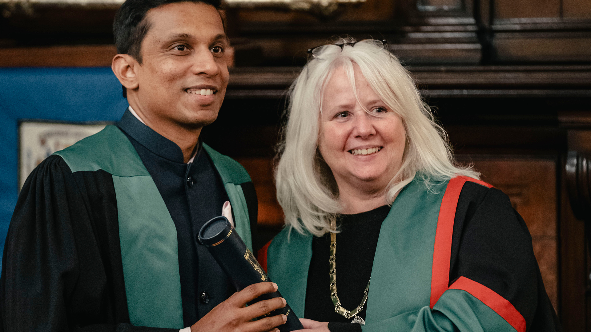 Two people smiling wearing black and green robes