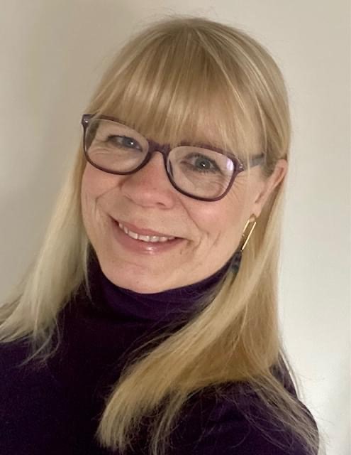 A woman with long blonde hair and glasses smiling
