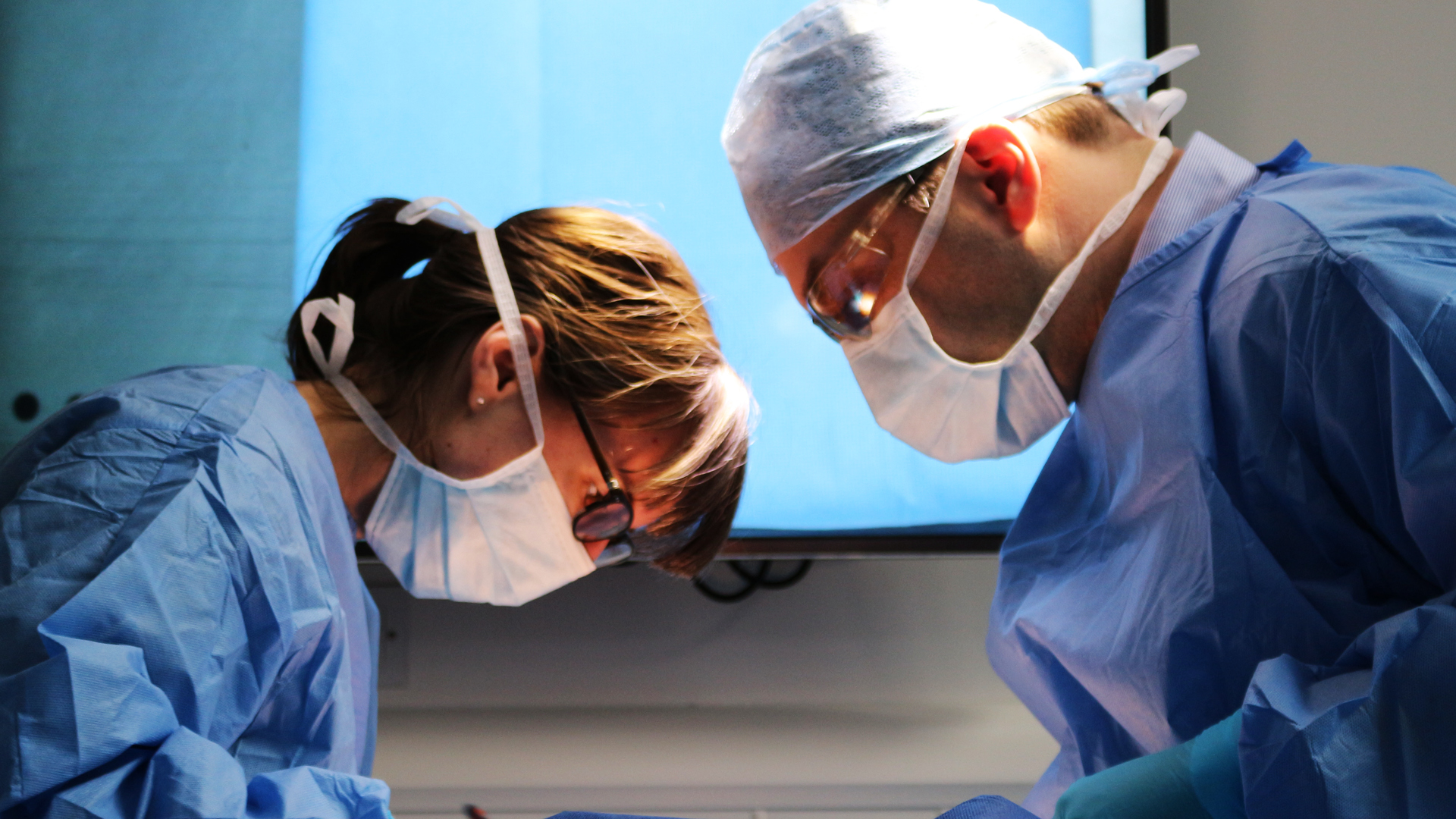 Two surgeons facing each other looking down towards a patient 